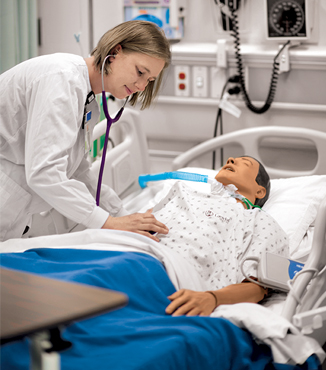 A nursing student trains in a practice lab with a life-sized dummy.