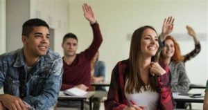students in college classroom. Three students raise their hands. 