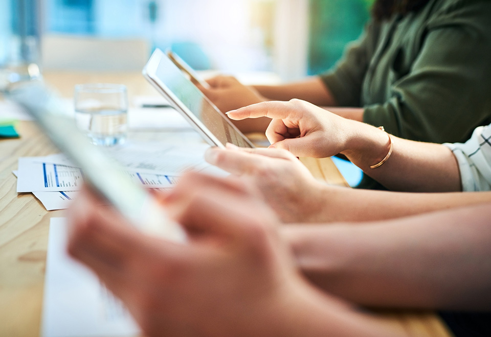 closeup of three business individuals reviewing information on tablets during a meeting